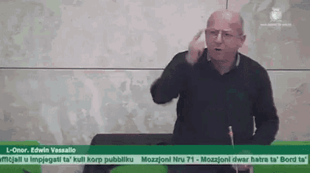 a man is sitting at a table giving a speech in a video .