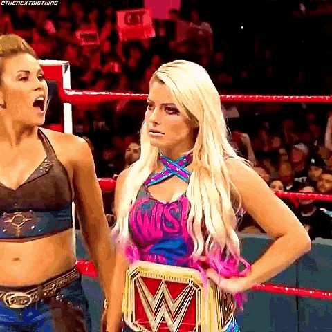 two women are standing in a wrestling ring and one has a wwe championship belt on her waist .