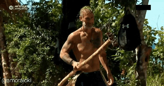 a man without a shirt is holding a stick in the woods .