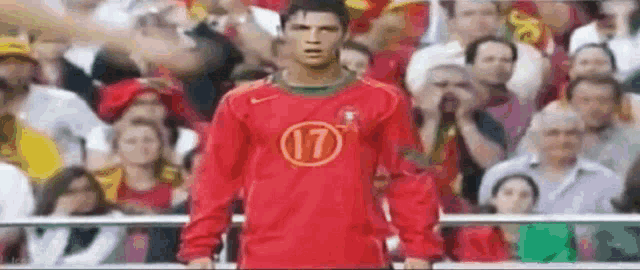 a soccer player wearing a red jersey with the number 17 on it is standing in front of a crowd of people .