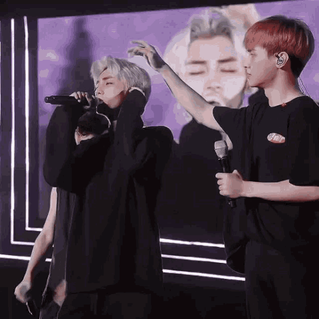 a man is holding a microphone while another man sings into it on a stage .