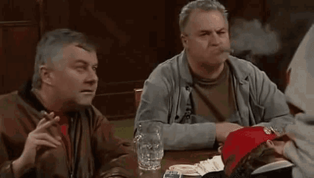 two men are sitting at a table smoking cigarettes .