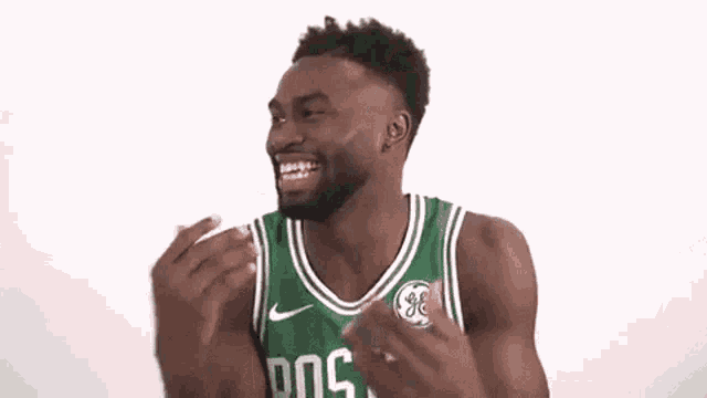 a man wearing a green and white boston celtics jersey is laughing with his hands in the air .