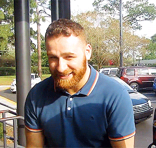 a man with a beard wearing a blue polo shirt stands in a parking lot