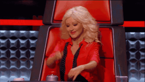a woman in a red shirt and tie is sitting in a red chair and dancing .