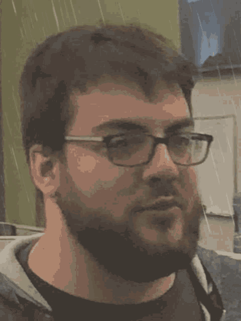 a man with glasses and a beard is standing in the rain