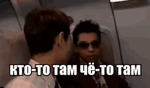 two men are sitting on a plane talking to each other . one of the men is wearing sunglasses .