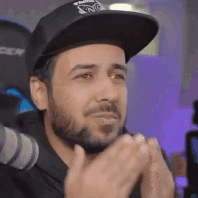 a man with a beard wearing a black hat is clapping his hands while sitting in front of a microphone .