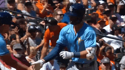 a baseball player wearing a blue jersey with the letter b on it is shaking hands with another player in front of a crowd .