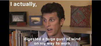 a man says " i actually digested a huge gust of wind on my way to work " in front of a bookshelf