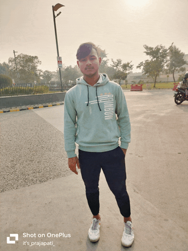 a man wearing a hoodie is standing in a parking lot with the words shot on oneplus written below him