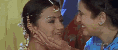 two women are touching each other 's faces and smiling in a video .