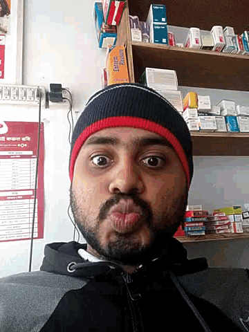a man with a beard wearing a black and red beanie stands in front of a shelf with extreme pleasure