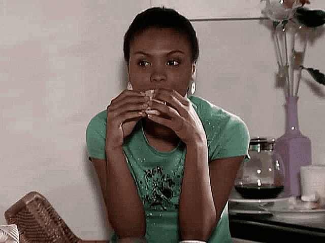a woman in a green shirt is eating a sandwich in a kitchen .
