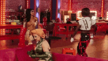 two drag queens are standing next to each other in a room with red lights .