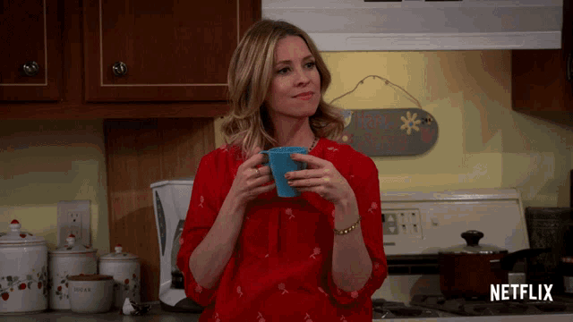 a woman in a red shirt is holding a cup of coffee in a kitchen with a netflix logo on the stove top