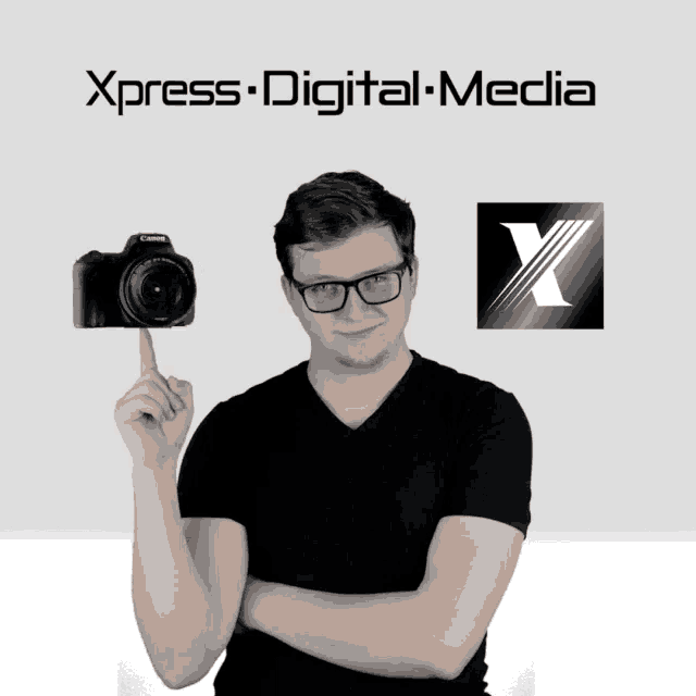 a man holds up a canon camera in front of a sign that says ' xpress digital media '