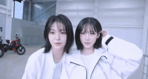 two girls are standing next to each other in a room with a motorcycle in the background