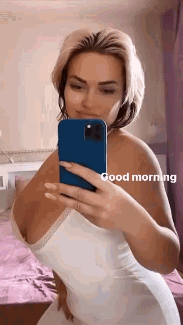 a woman in a white dress is taking a selfie with a blue phone .