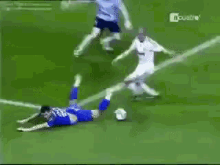a soccer player is laying on the ground while another player tries to catch the soccer ball