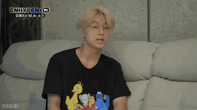 a man sitting on a couch wearing a black t-shirt that says enhypen