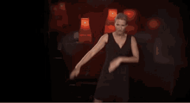 a woman in a black dress is dancing on a stage in front of red lamps .