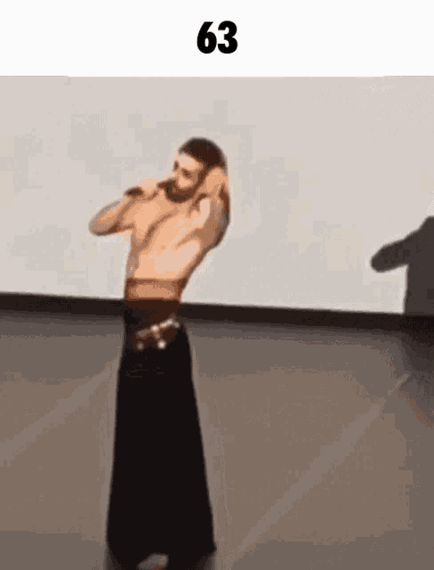 a man without a shirt is dancing on a stage in a long black skirt .