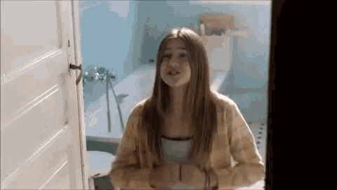 a girl is standing in a bathroom next to a bathtub and toilet .