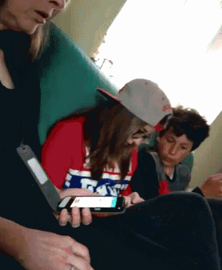 a girl in a red white and blue shirt with the letter t on it looks at a cell phone