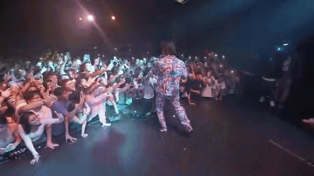 a man in a colorful shirt is standing on a stage with a crowd behind him .