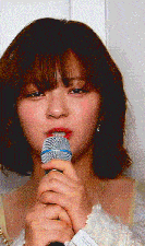 a woman is singing into a microphone while wearing a white shirt