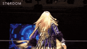 a woman in a purple and gold outfit is dancing in front of a stardom logo