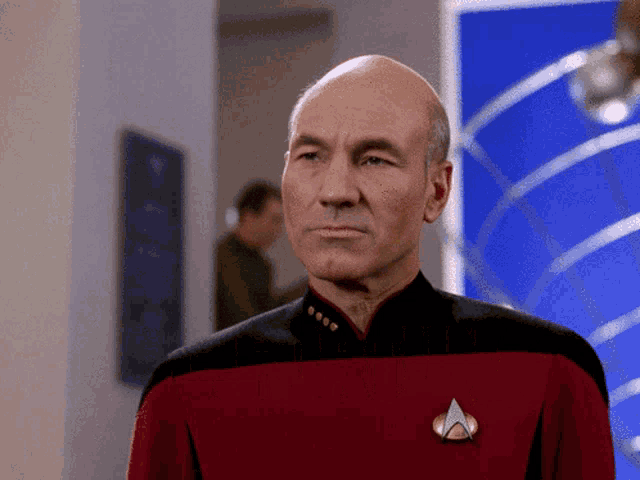 a bald man in a red and black uniform with a star trek badge on his chest