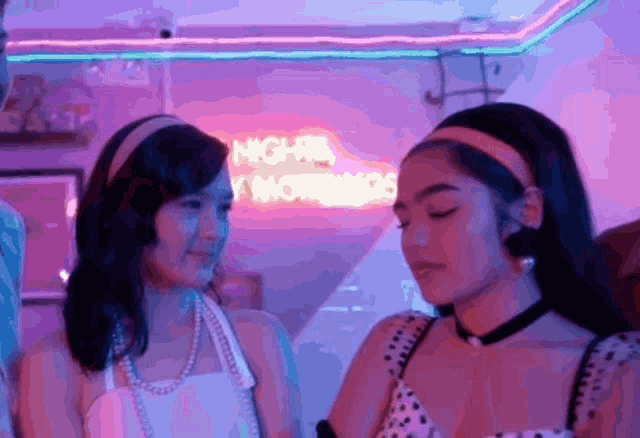 two women are looking at each other in front of a neon sign that says night is my morning