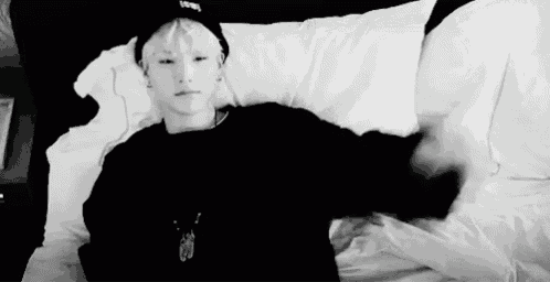 a black and white photo of a person laying on a bed with a hat on .
