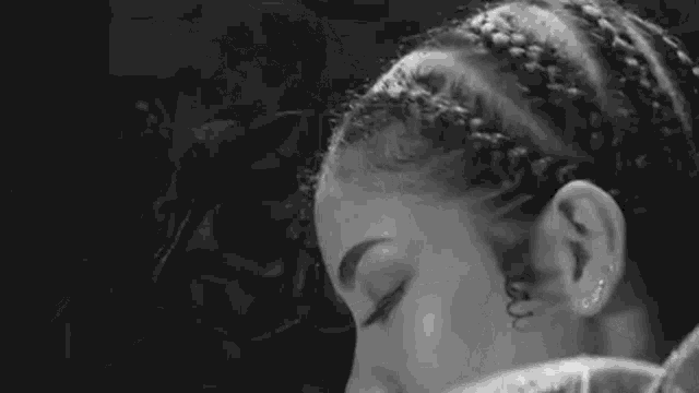 a black and white photo of a woman with braids covering her face with her hand .