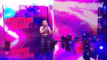 a woman singing into a microphone on a stage with the name jordynne grace on the screen behind her