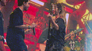 a woman singing into a microphone while a man plays a guitar on stage .