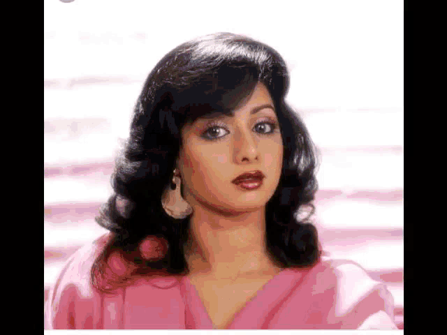 a close up of a woman 's face with a pink shirt and earrings .