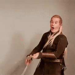 a man in a hobbit costume is holding a sword and making a funny face .