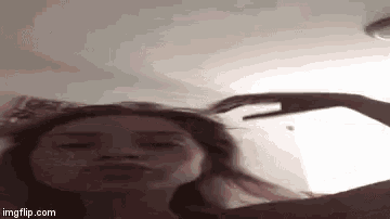 a woman is making a funny face with her hand while laying on a bed .