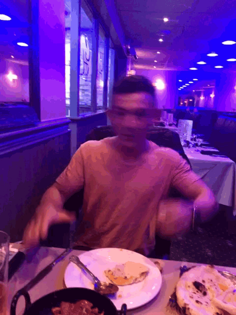 a man sitting at a table in a restaurant with purple lights behind him