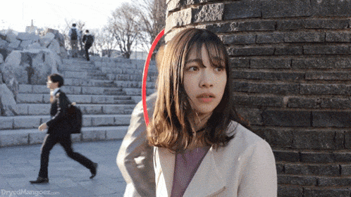 a woman is standing in front of a brick wall with a red arrow pointing to her head