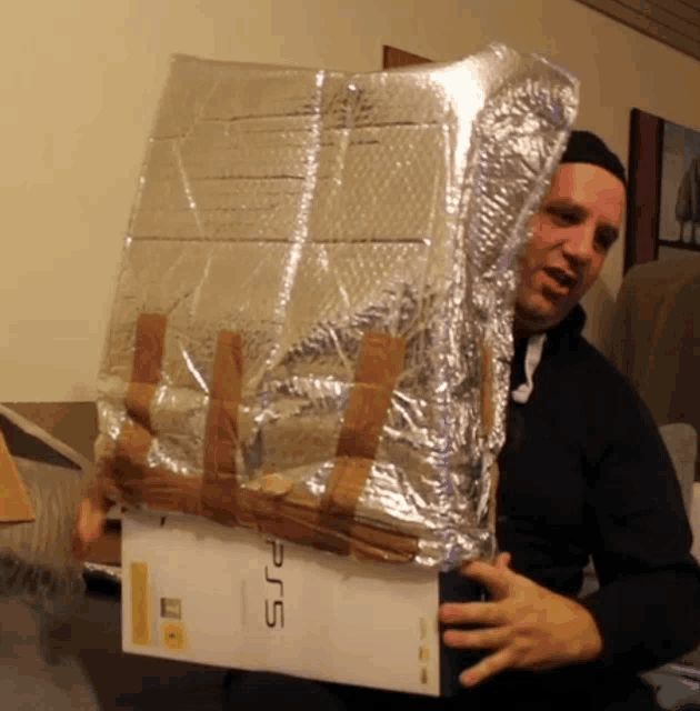 a man is holding a ps5 box wrapped in foil