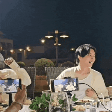 a group of people are sitting at a table with their cell phones on their lap