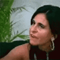 a woman wearing hoop earrings is sitting on a couch and making a face .