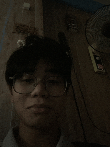 a man wearing glasses is standing in front of a fan and a sign that says ' a ' on it