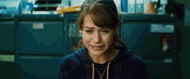 a woman in a blue hoodie is crying in front of a row of filing cabinets