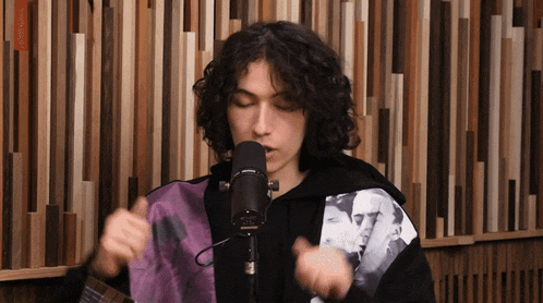 a young man with curly hair is singing into a microphone in front of a wooden wall