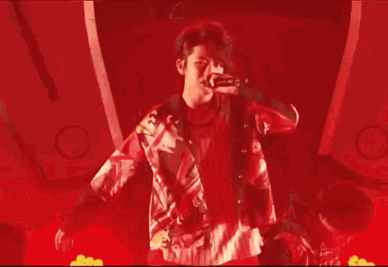 a man is standing in front of a red background with his arms up in the air .